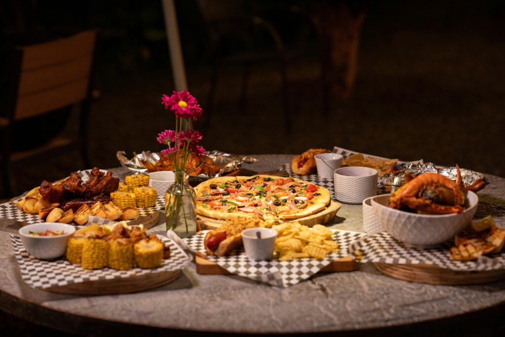 A diverse dinner spread with pizza, corn, ribs, and snacks on an outdoor table setting.
